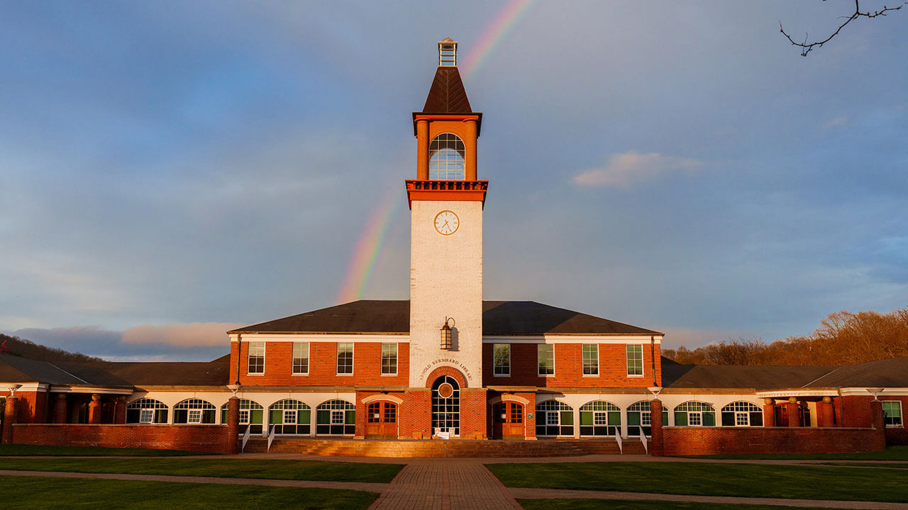 arnold bernhard library is lit up with golden light from a sunset with a rainbow behind it