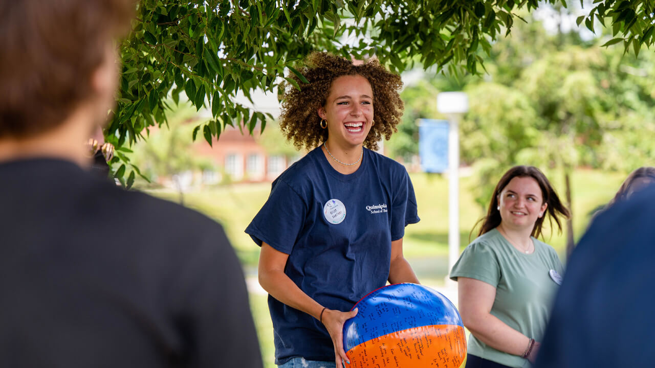 An Orientation leader smiles broadly as she holds a beachball covered in writing