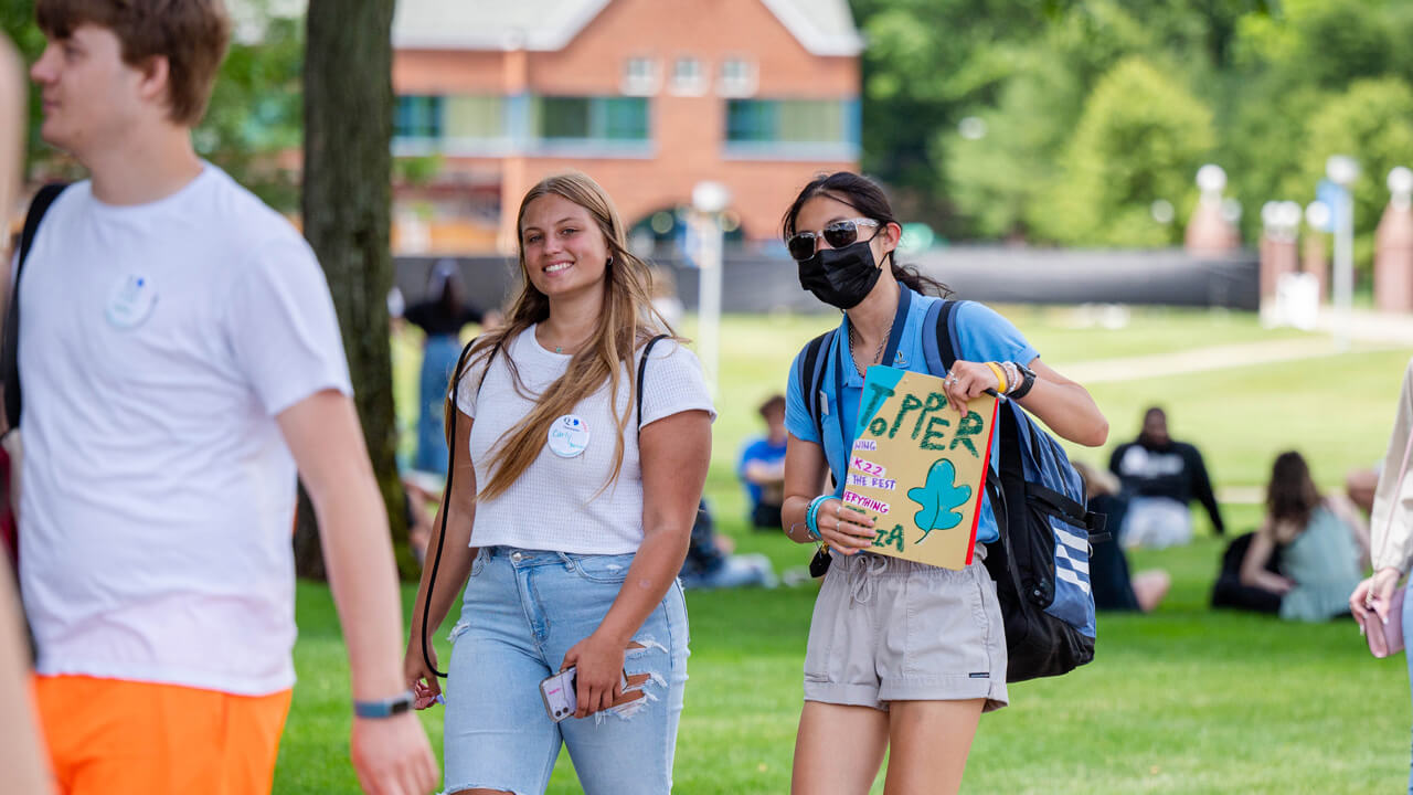 An Orientation leader and a new student smile for a photo as they walk across campus
