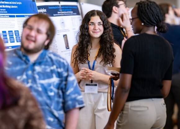 Photo of Sophia Vigorito standing in front of poster and looking at a female listener