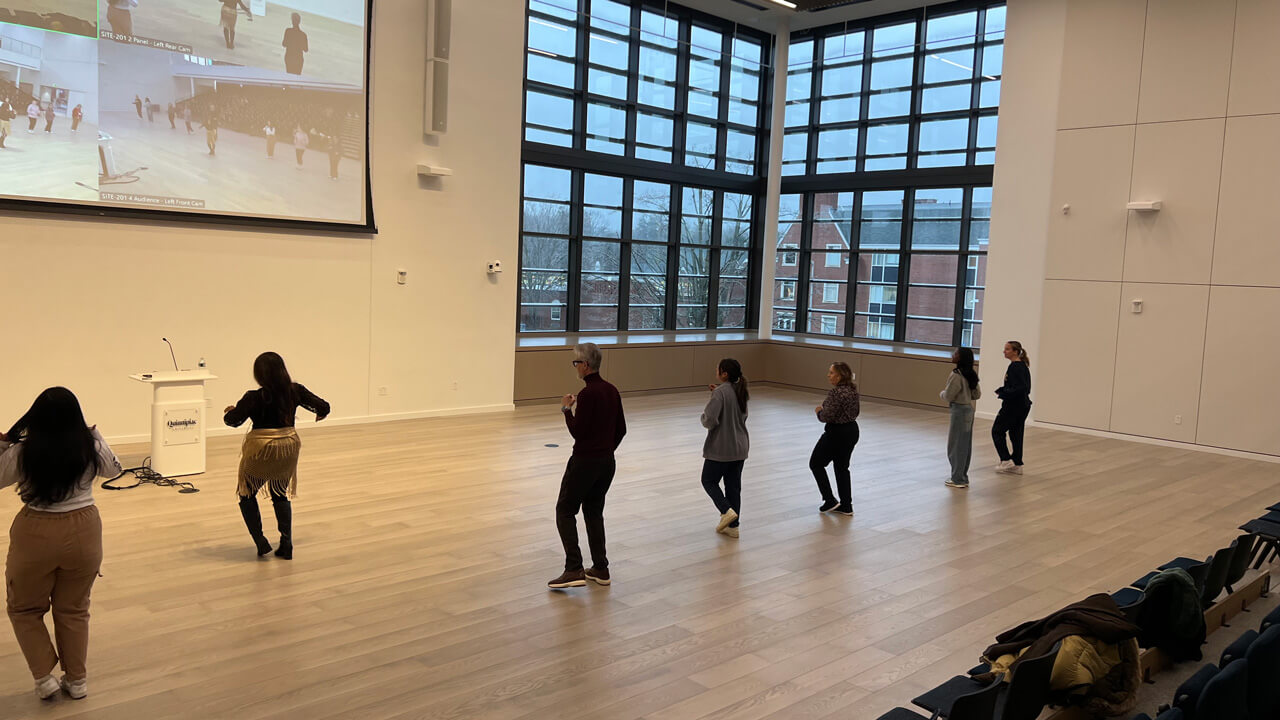 A wide shot of student and faculty participants with the instructor in front demonstrating a move.