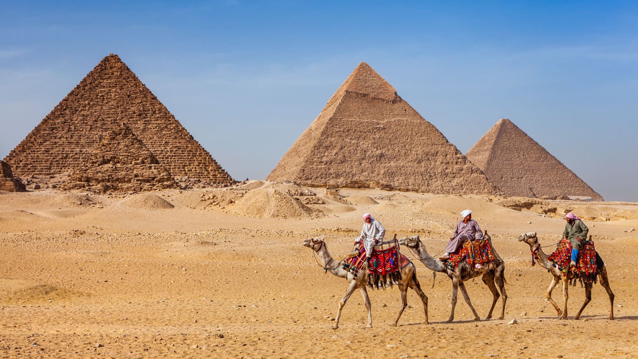 Desert and pyramids with men riding camels