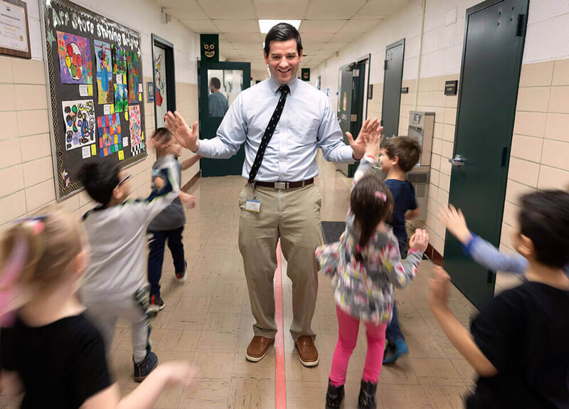 An education alum hi-fives students as they pass in a hallway in a Milford elementary school