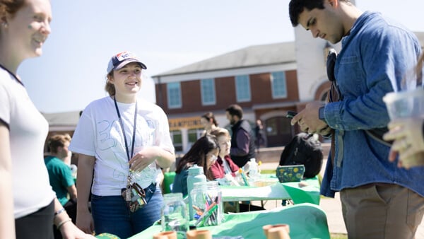 Three students talk next to a table with small pots and seed packets during the Earth Day celebration at Quinnipiac