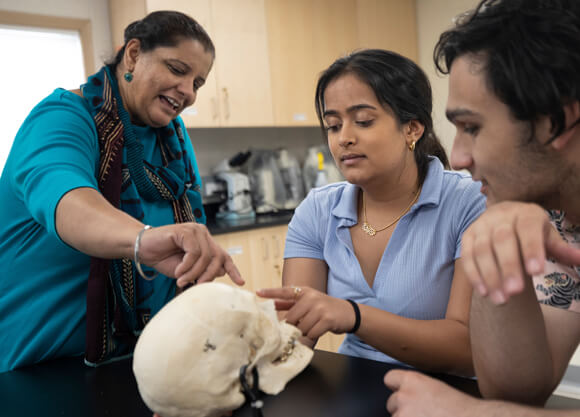 Two students and a professor examine a human skull at a lab table