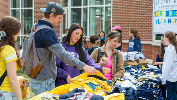 Students look at shirts on a table at an outdoor flea market on the Quad
