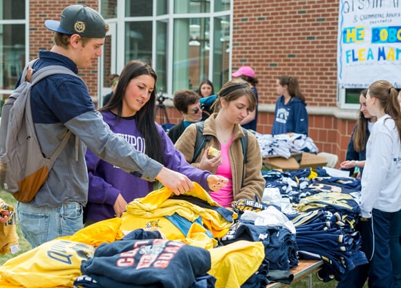 Students look at shirts on a table at an outdoor flea market on the Quad