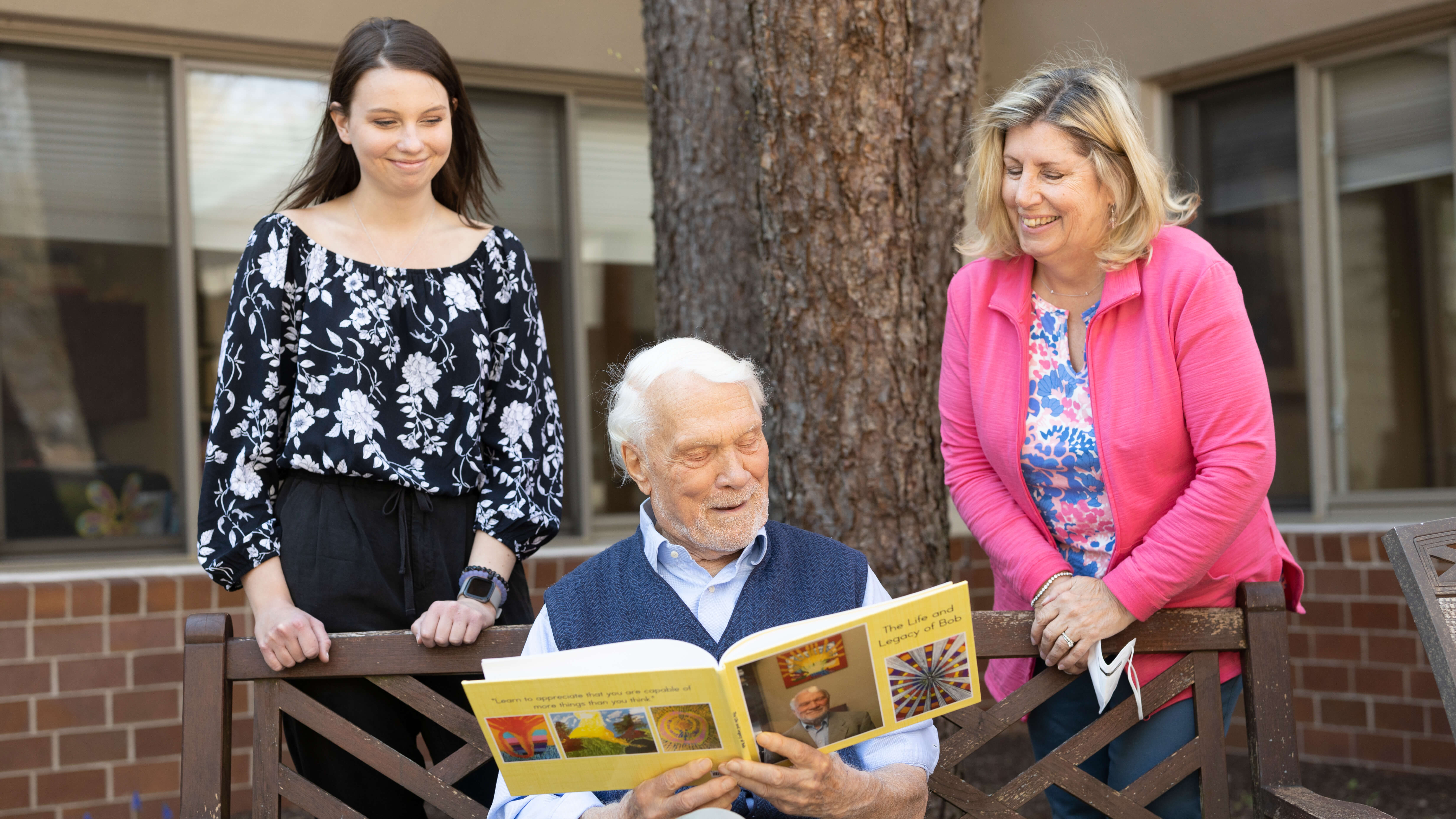 Bob Savage, a resident of LiveWell Dementia Specialists facility, reads from his Legacy book to volunteers Jessica Leach and Janet Waldman