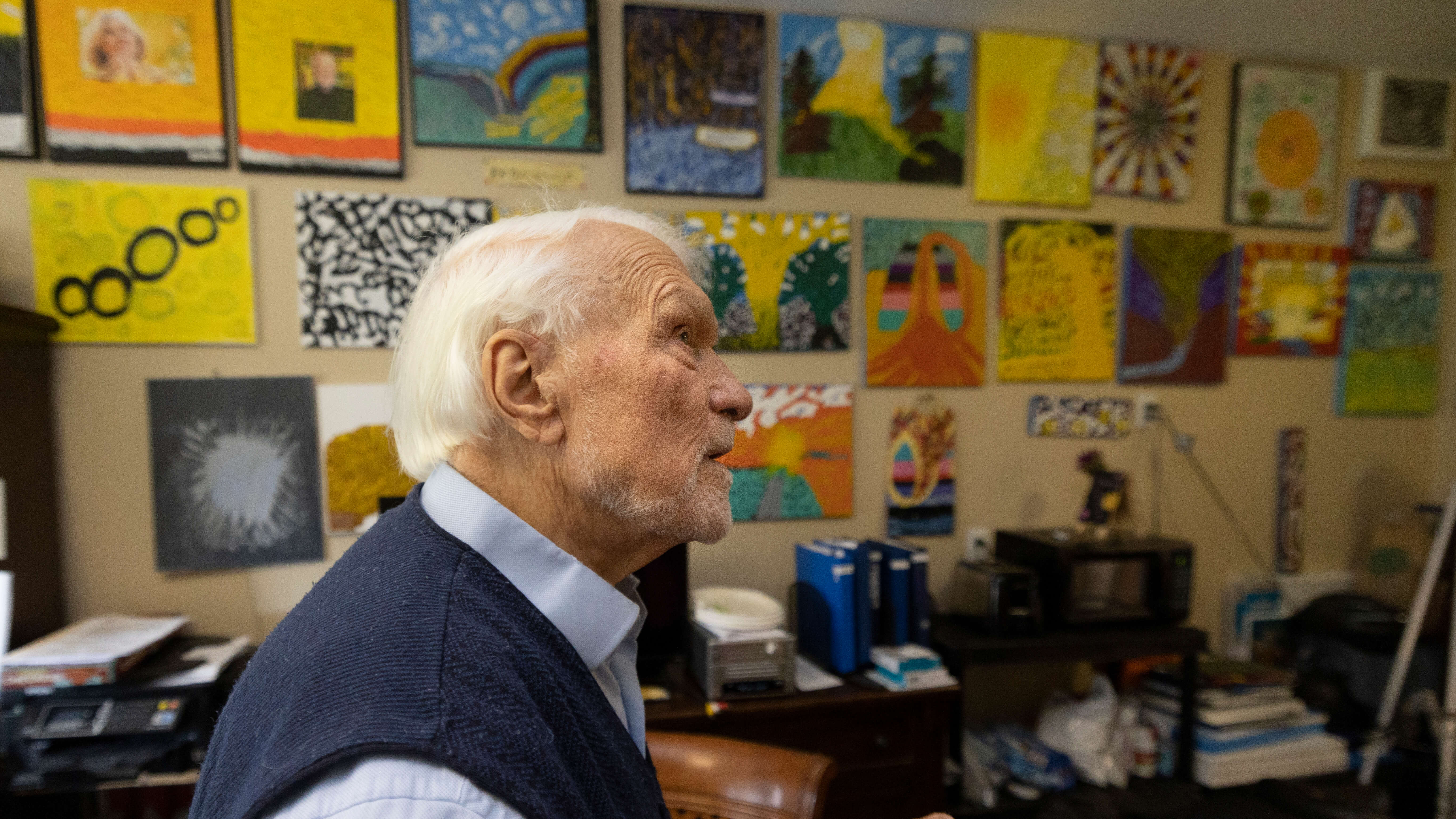 Bob Savage sitting in his home surrounded by paintings he has created
