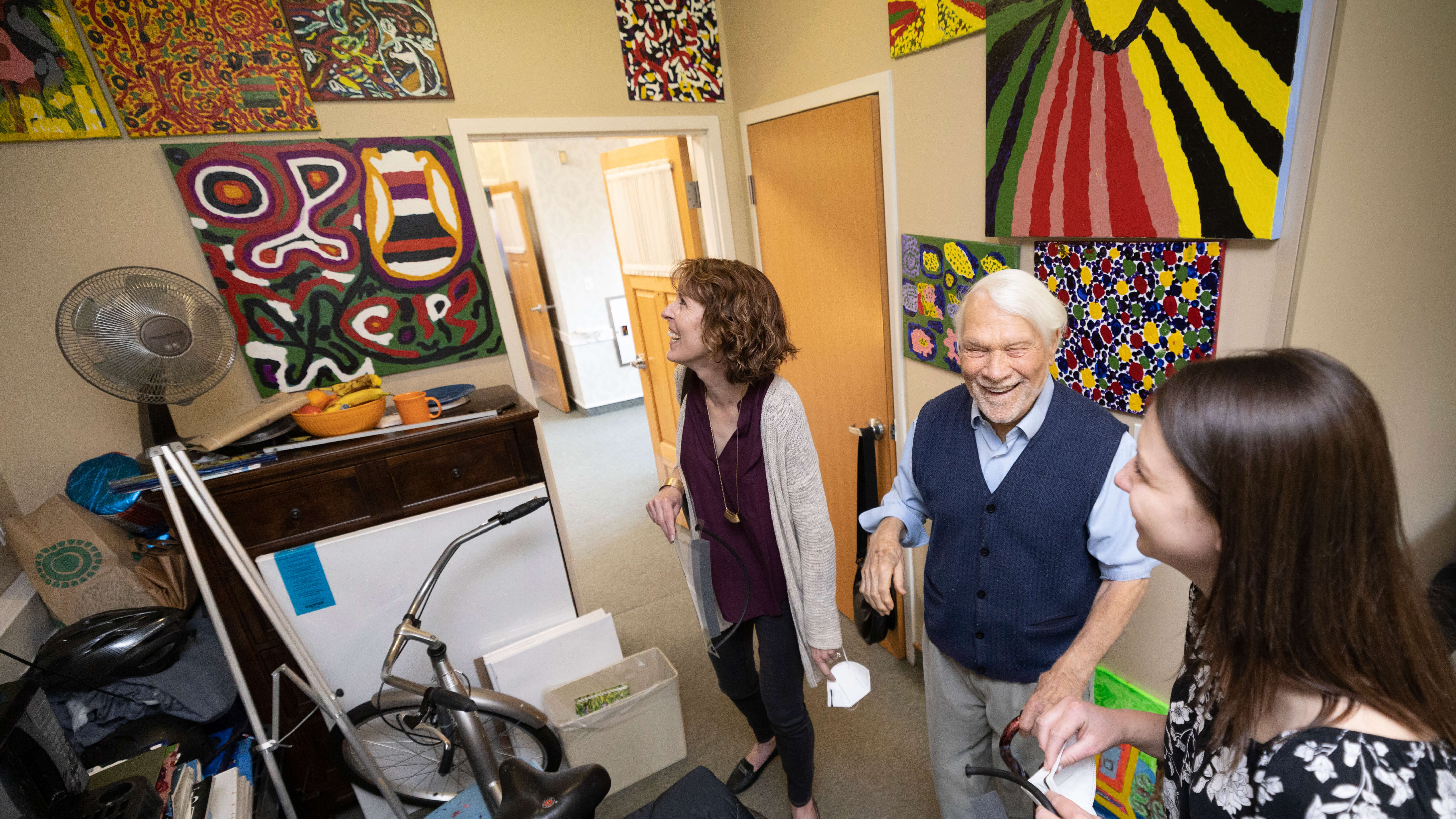 Bob Savage, a resident of LiveWell Dementia Specialists facility, shows volunteers Norene Carlson, Clinical Assistant Professor of Occupational Therapy, and Jessica Leach,  a junior OT student, his artwork