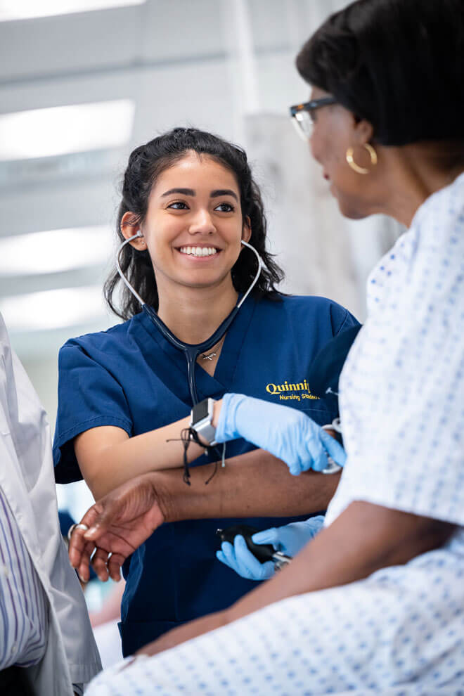 A nursing student smiles while helping a patient.