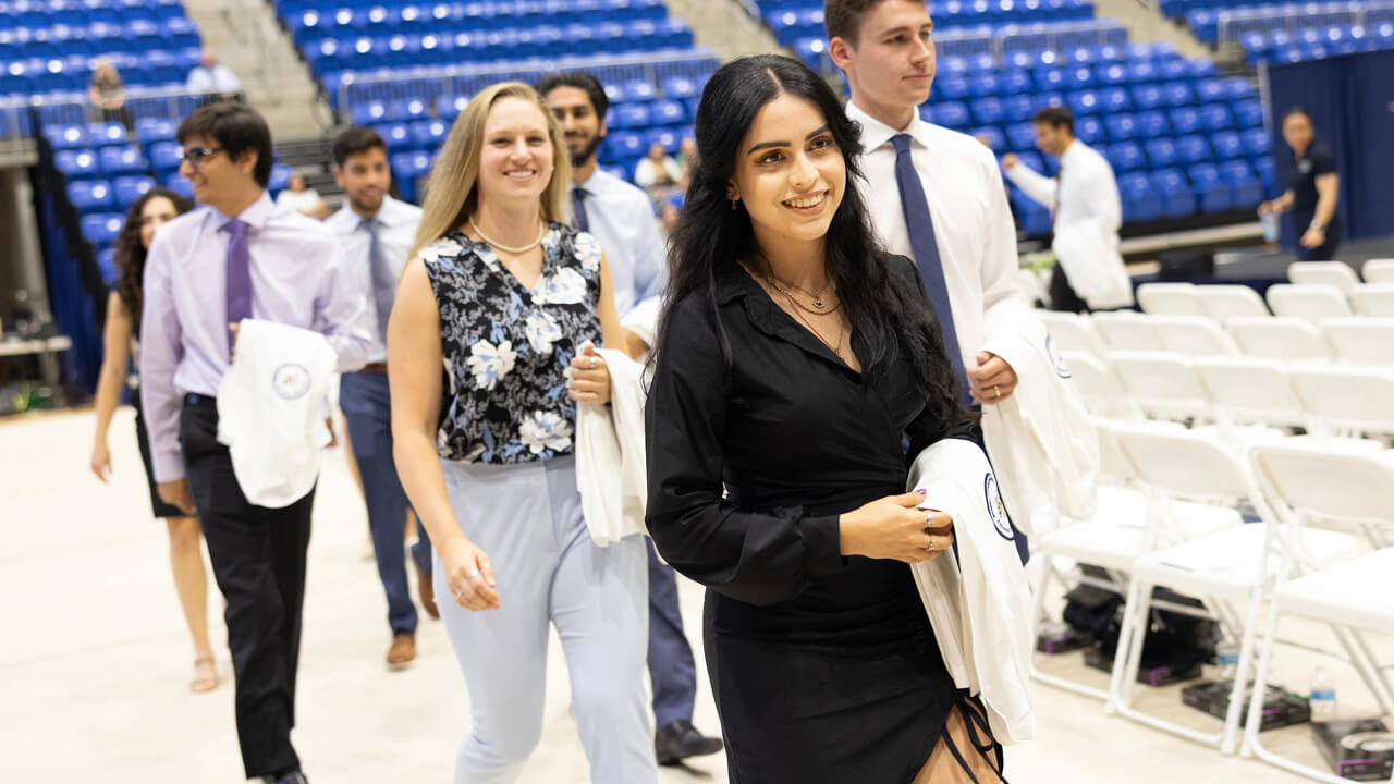 Half a dozen new medical students walk into the ceremony with their white coat over their arms
