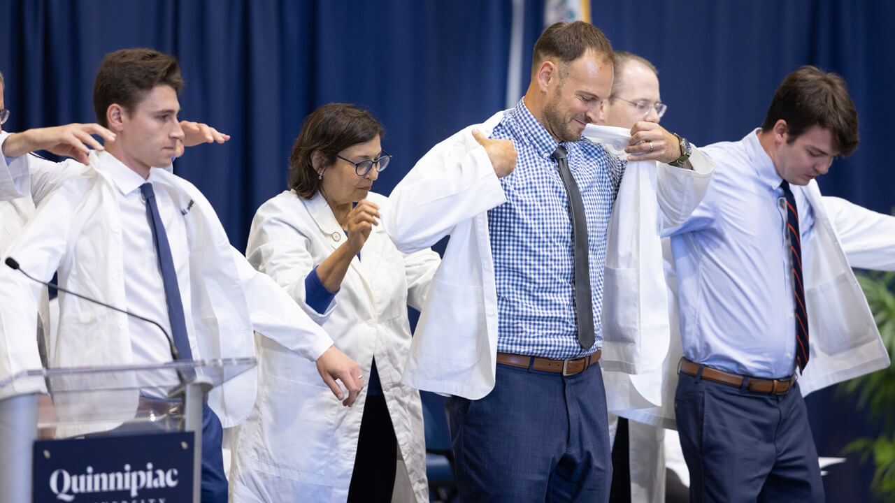 Three new medical students put on their white coats on the stage