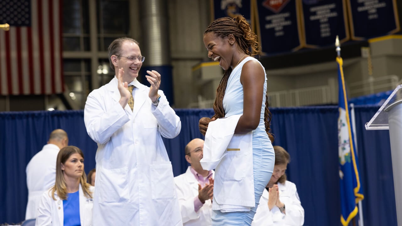 A student laughs as she walks onto the stage with her white coat on her arm