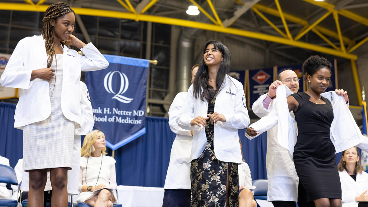 New medical students smile at each other as they put on their white coats