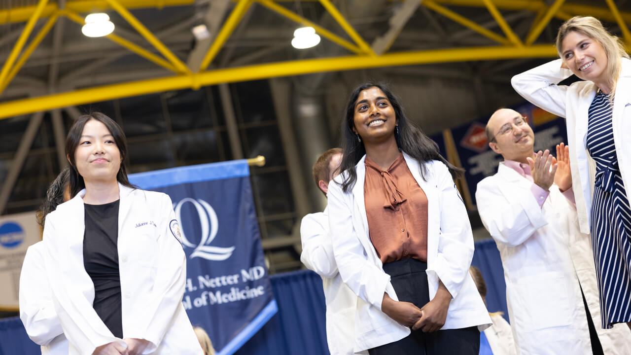 Three new medical students smile for a photo on stage