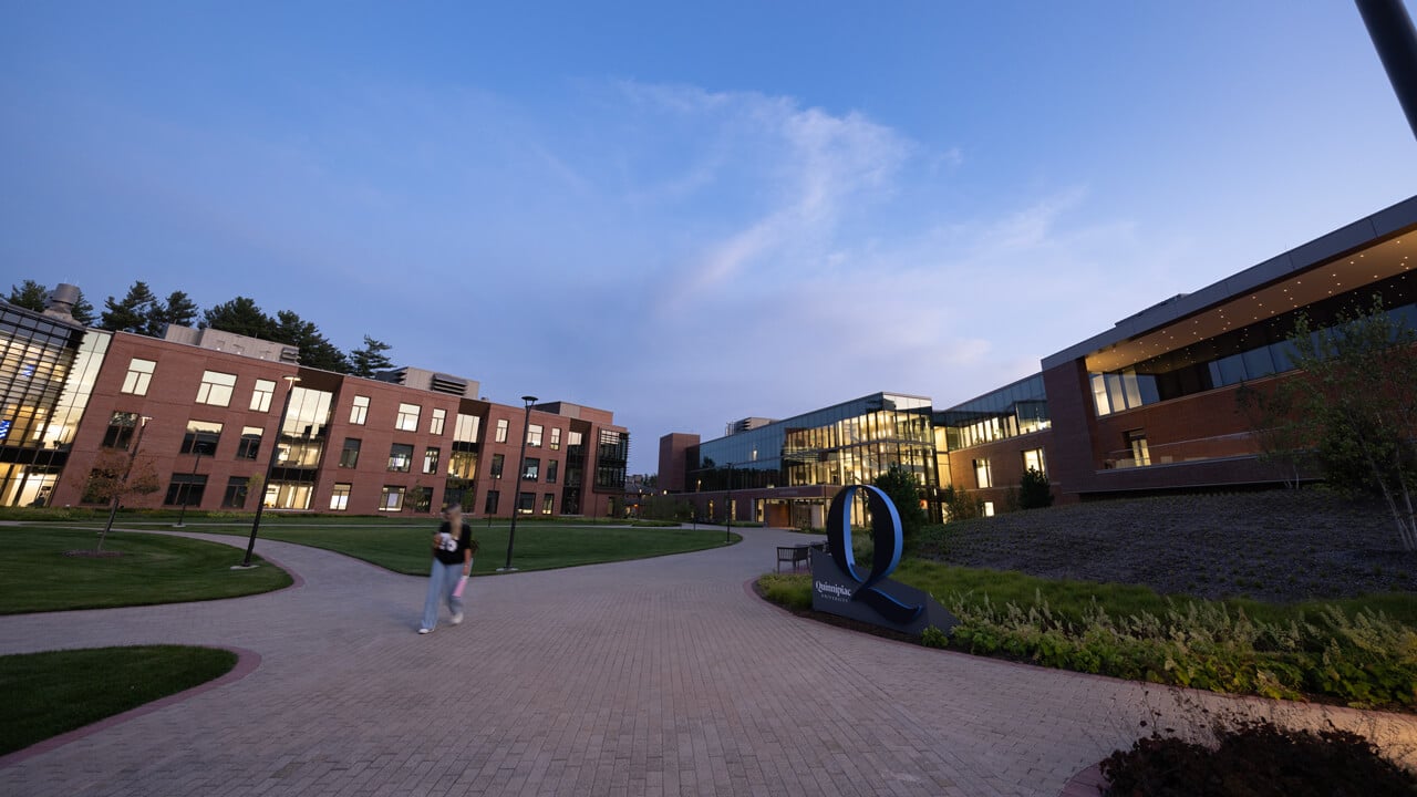 A student walks across the South Quad with the buildings aglow during evening