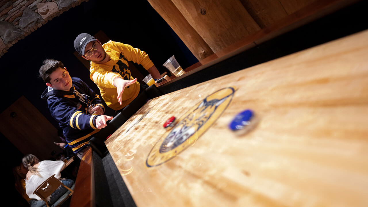 Two students play tabletop shuffle board in the pub
