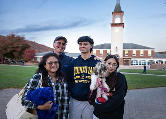 A Quinnipiac family takes a picture in front of the library during Bobcat Weekend 2024.