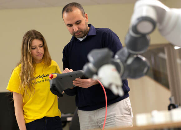 An engineering student and professor use the remote control for a robot.