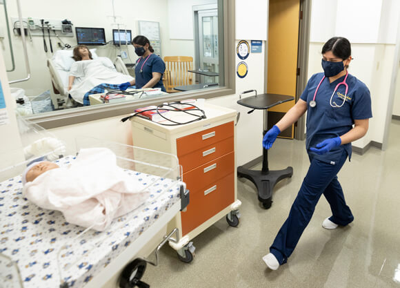 Quinnipiac nursing student walks through the mock hospital with mannequin patients.