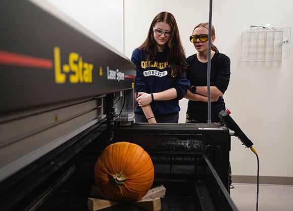 Students use a laser machine to carve a "Q" in a pumpkin