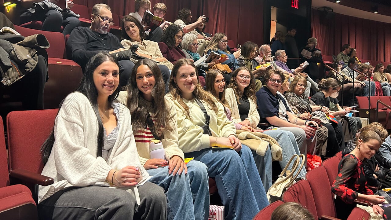 A group of six students smiling, sitting in a row in the theatre.