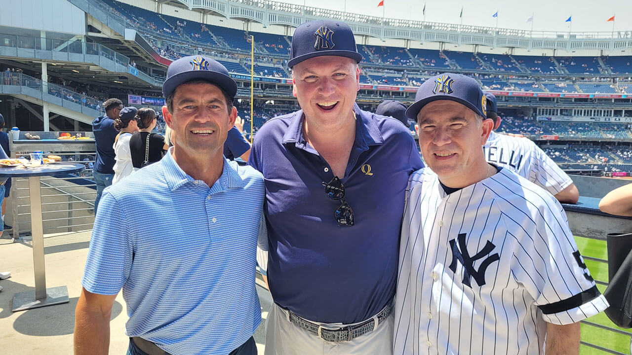 Three alumni take a photo in front of the Yankee baseball field