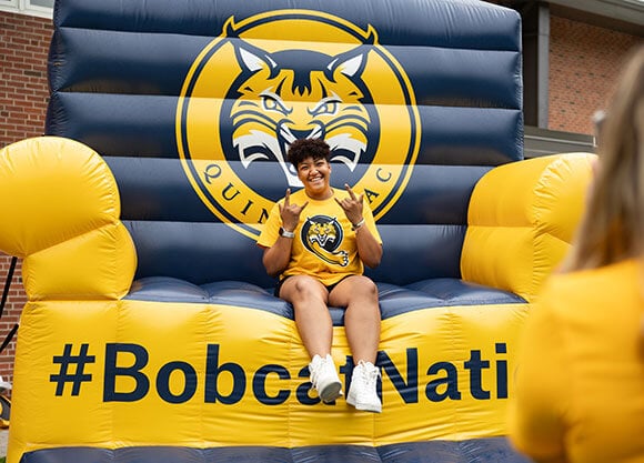 Student in a bobcat t-shirt posing on a gold and blue BobcatNation inflatable seat