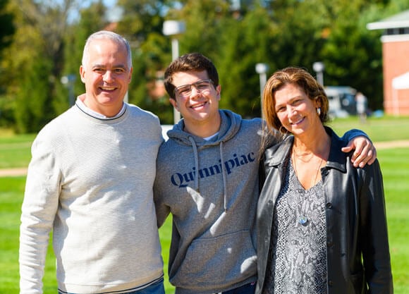 A student smiles with his parents during parents and family weekend