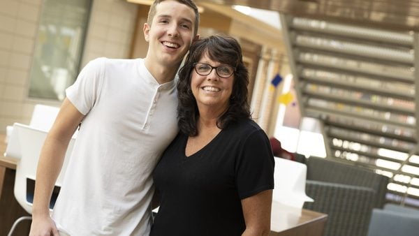 A smiling student and parent stop and smile together in a bright residence hall atrium
