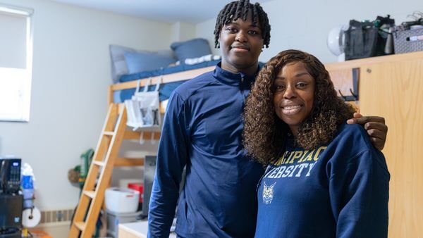 A new student and mother smile in front of his newly moved-in dorm room