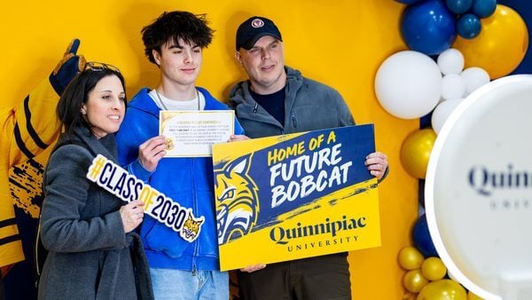 A future Bobcat poses proudly with his parents at a Quinnipiac photo booth