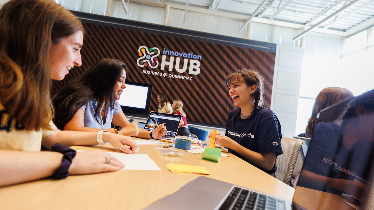 A dozen students collaborate at tables in the Innovation Hub in the School of Business