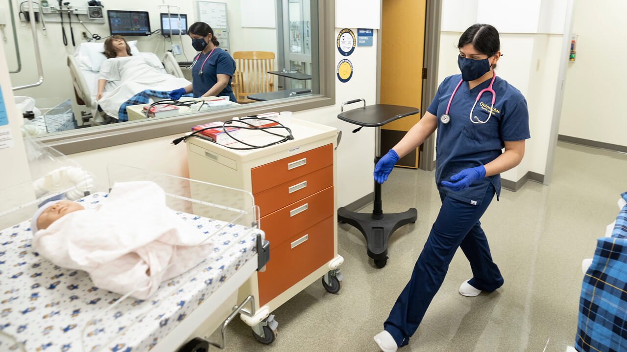 A nursing student attends to a manikin in a hospital simulation room