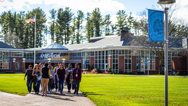 A tour group walks across the quad with the student center behind them on a sunny day