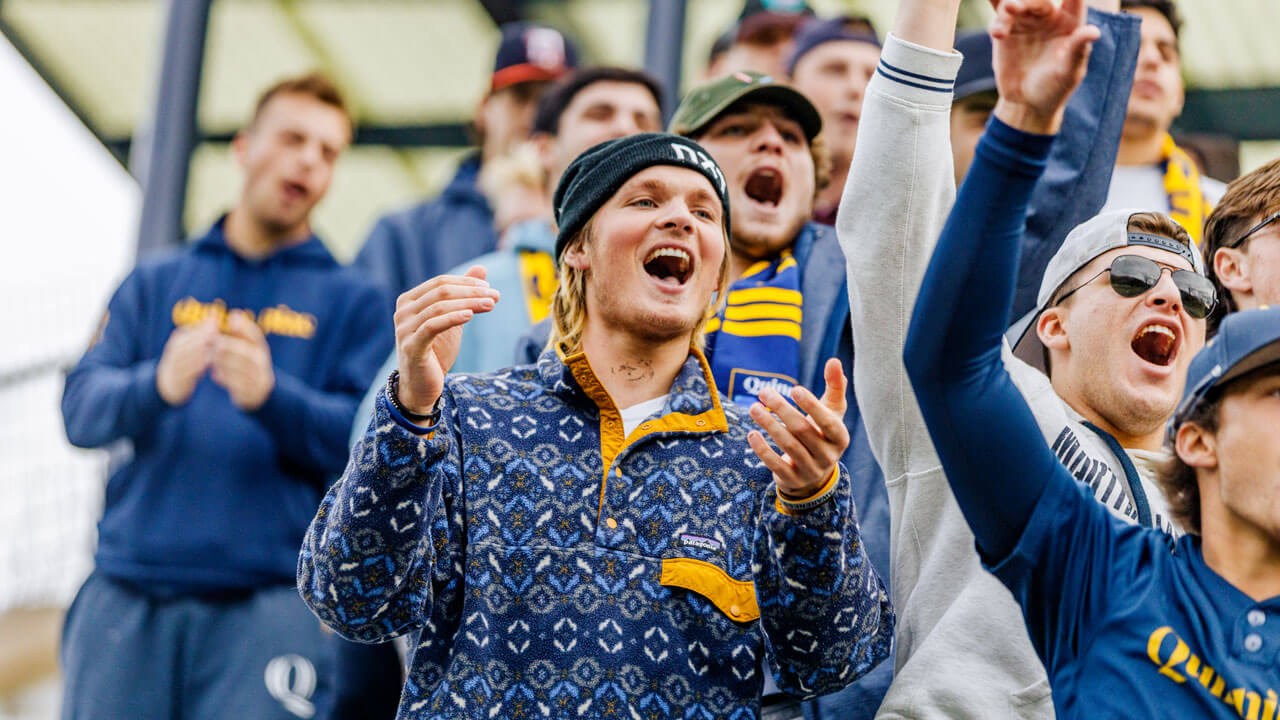 Students decked out in navy and gold Quinnipiac colors, cheering on the women's soccer team