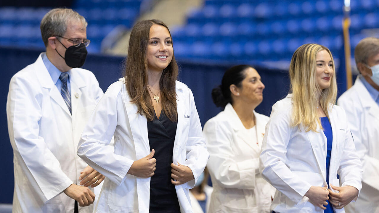 Medical graduates stand on stage proudly wearing their white coats