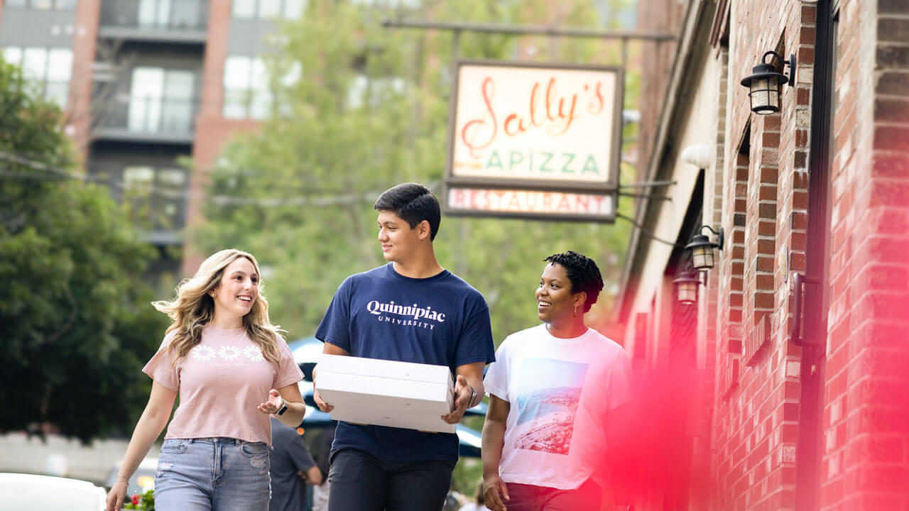 Students walk around New Haven holding a pizza box