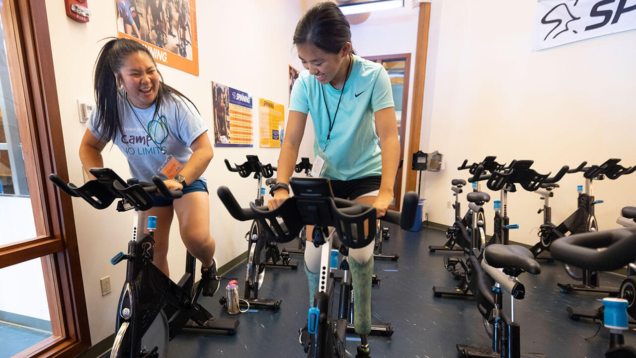 Student teaches a camper on a spin bike