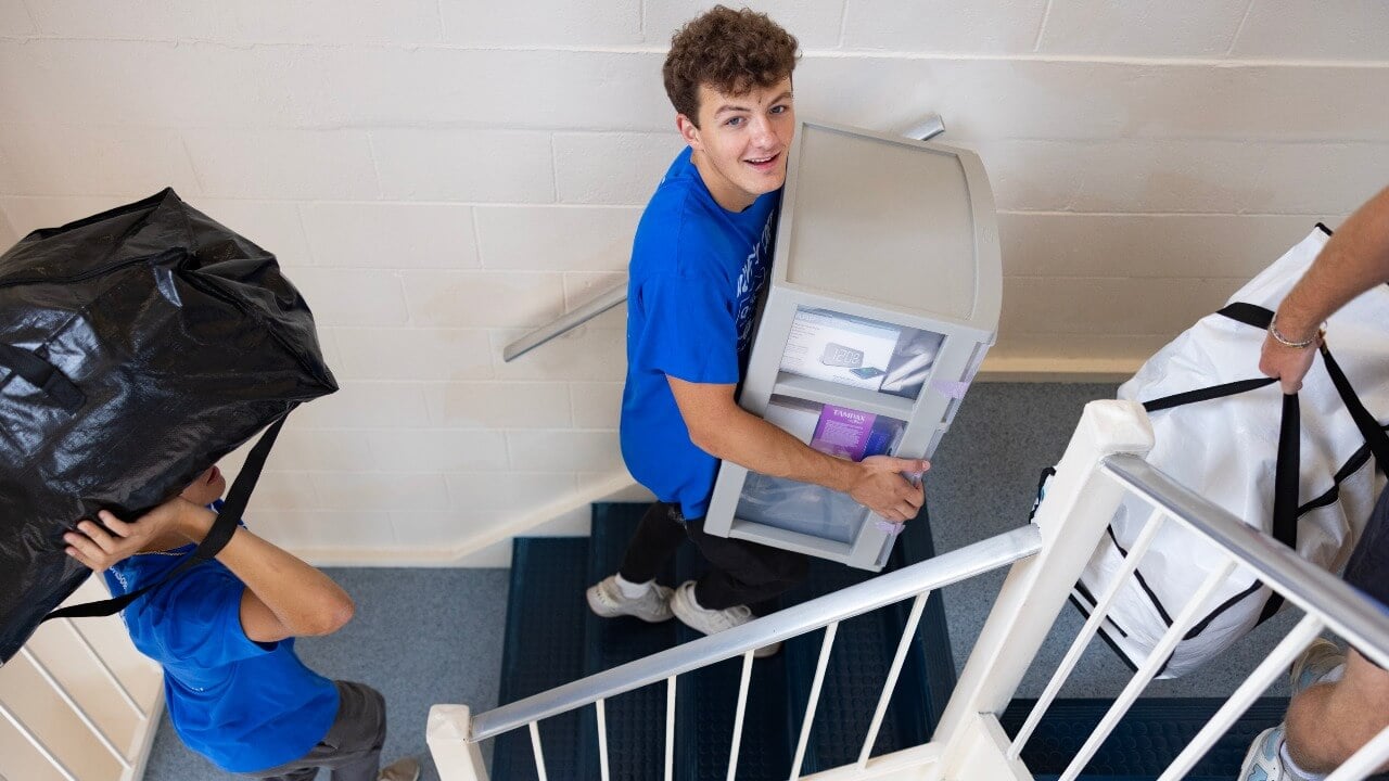 Students carrying move-in bags up stairs