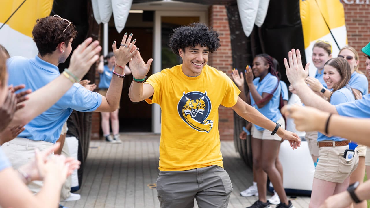 A new Quinnipiac student walks through 2 cheering lines of orientation leaders giving a high five at undergraduate orientation