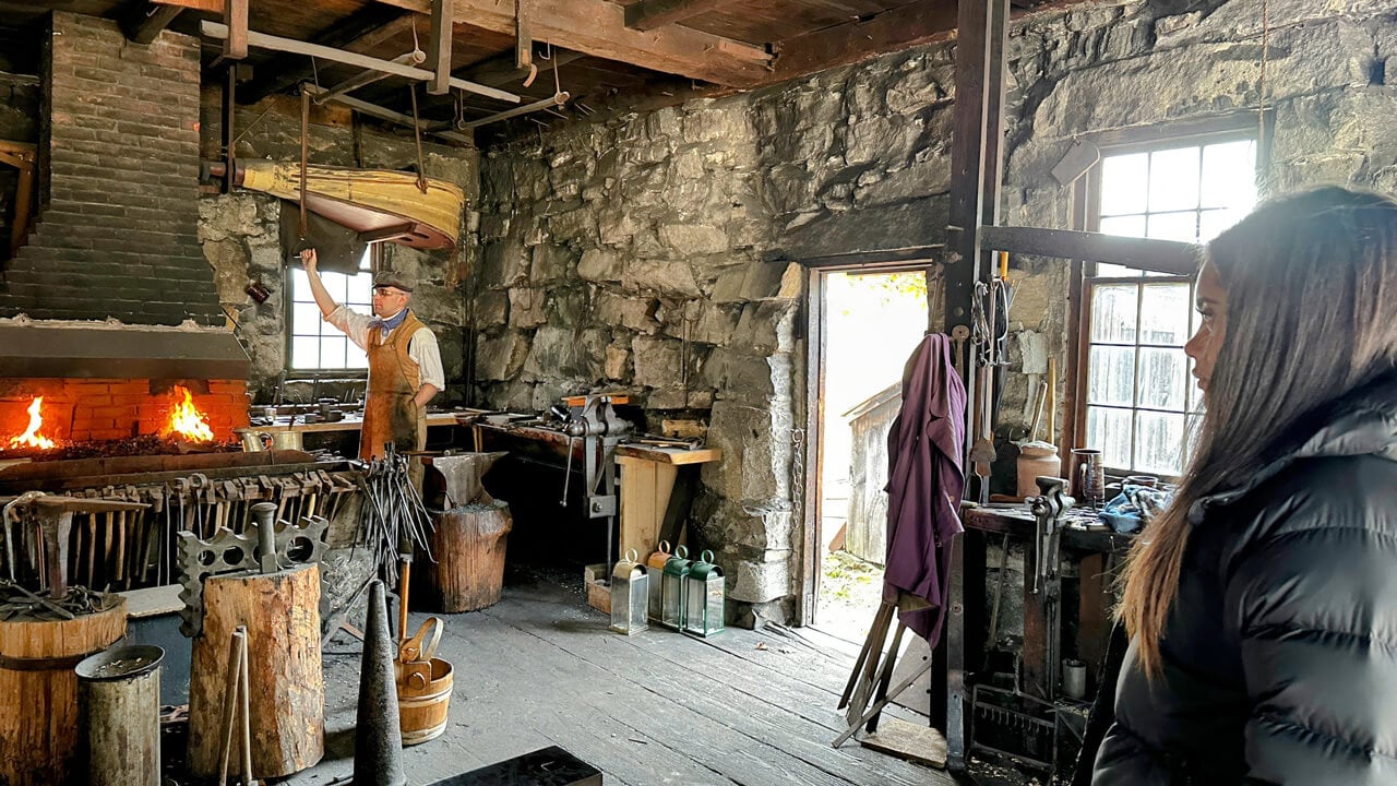 A student in a puffer jacket watching a metalworking demonstration.