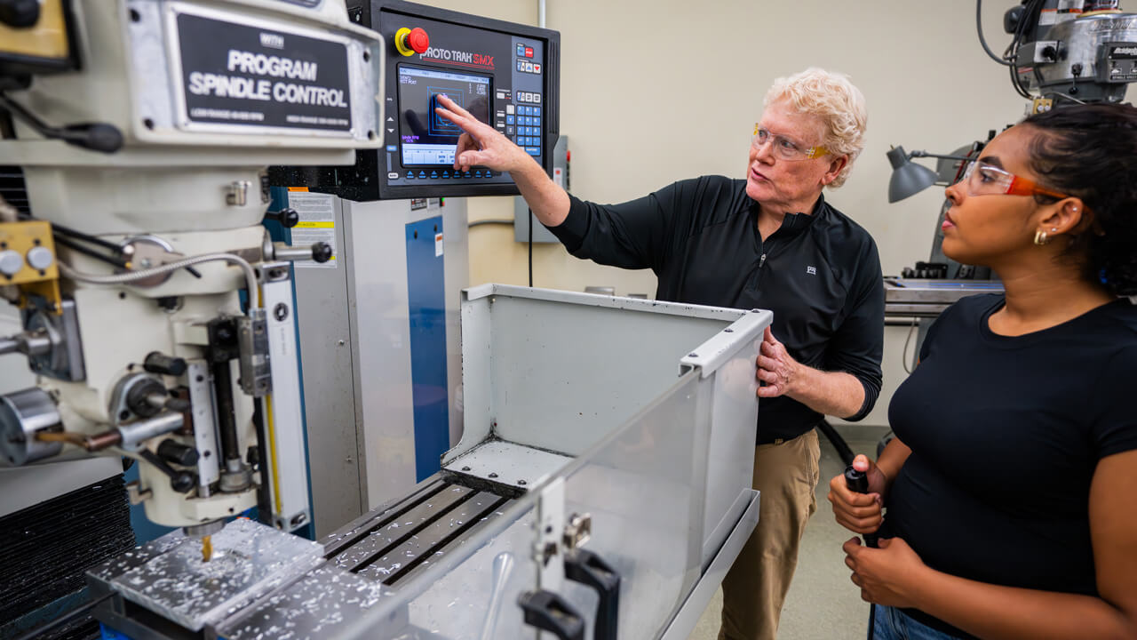 A close-up of machine shop machinery with a blurred background of a female student.