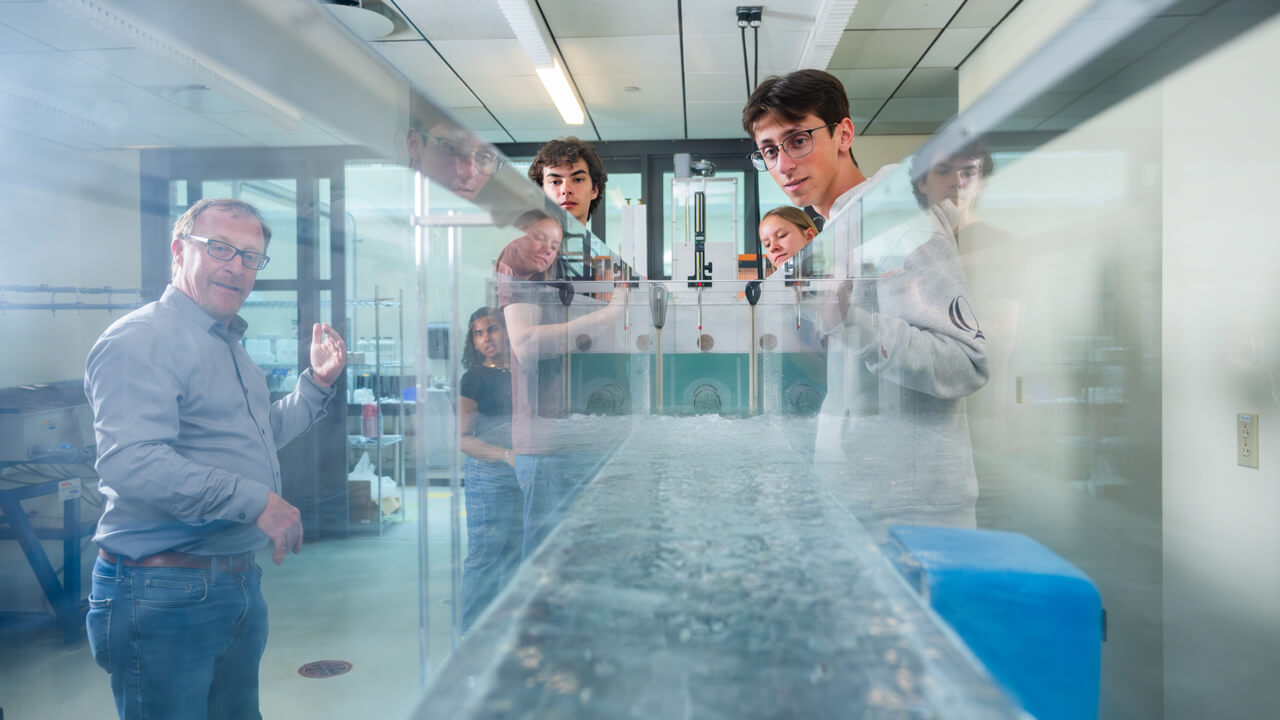 A head-on shot of a fluid tank with faculty and students looking into it on either side.