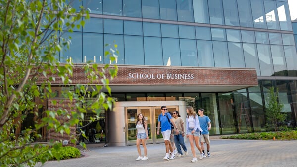 A group of students walk together in front of a wall of windows on the School of Business building