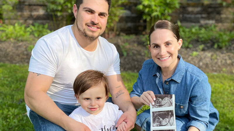 Alicia and Robert Maione hold an ultrasound print out and smile with their toddler