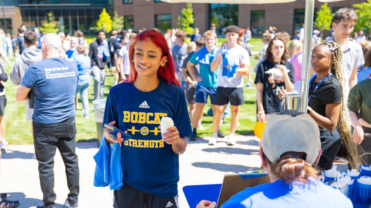 Student holds ice cream in front of a crowd of people on South Quad