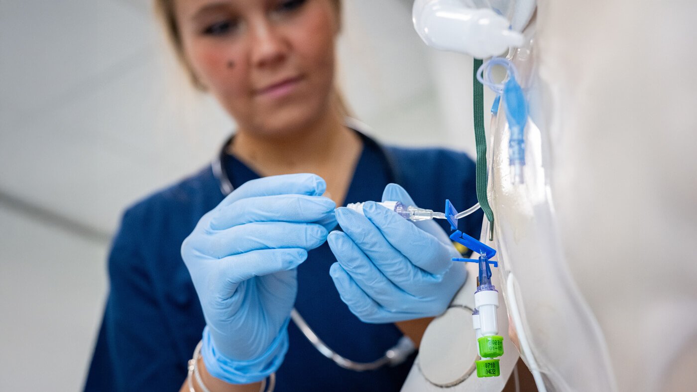 A Quinnipiac nursing student wearing gloves practices inserting an IV line on a medical mannequin during simulation training.