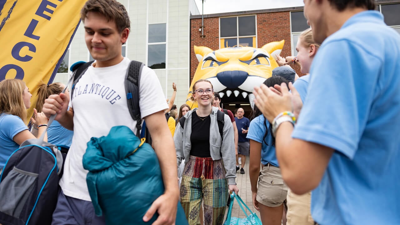 New students carry bags as staff and students cheer for them during Orientation